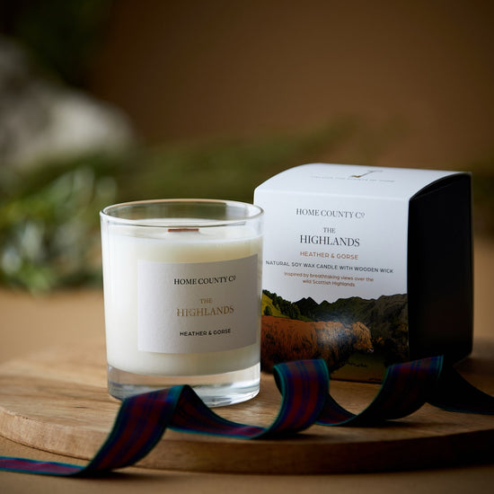 A Scottish Highlands candle from the Home County Co is shown next to the Highland Cow illustrated candle box