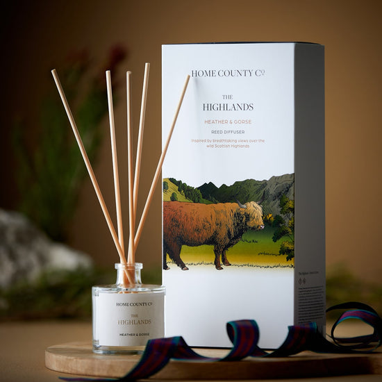 A Highlands heather and gorse reed diffuser from the Home County Co. is shown next to its eco-friendly illustrated reed diffuser box
