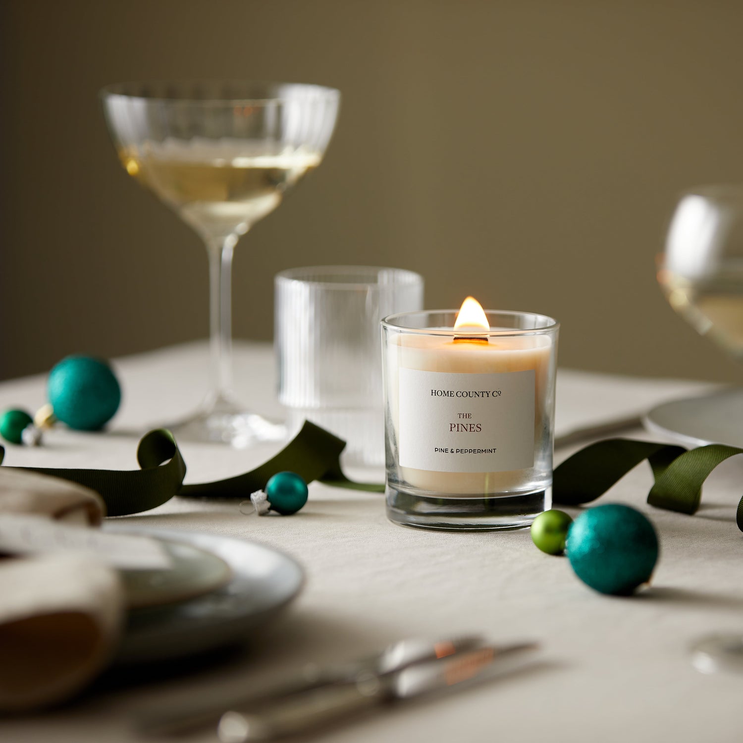 A pine and peppermint scented candle from the Home County Co. is shown alight on a Christmas table 