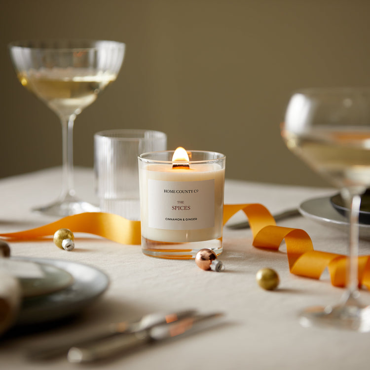 A cinnamon and ginger scented candle from the Home County Co. is shown alight on a Christmas table 