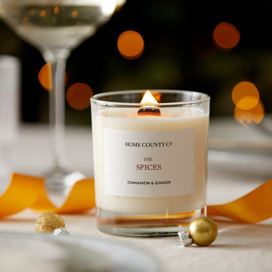A cinnamon and ginger scented candle from the Home County Co. is shown alight on a Christmas table 