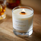 A scotch whisky scented candle from the Home County Co is shown with its wooden wick lit