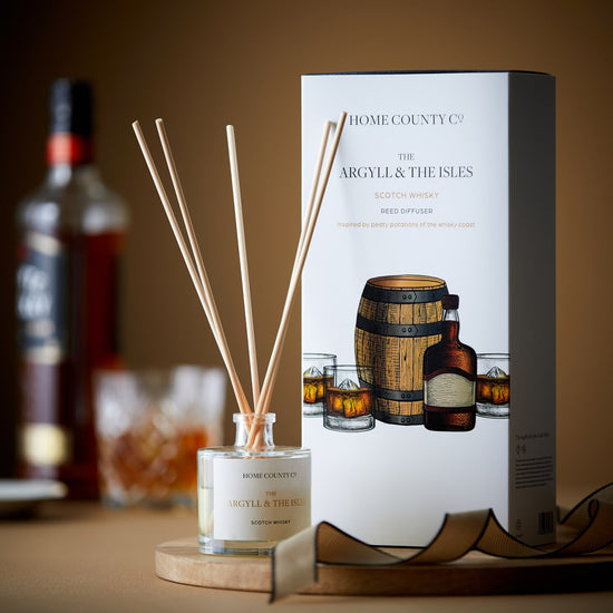 A scotch whisky scented reed diffuser from the Home County Co is shown next to the eco-friendly illustrated packaging
