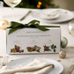 A Christmas candle gift set is shown as a place setting on a Christmas themed table